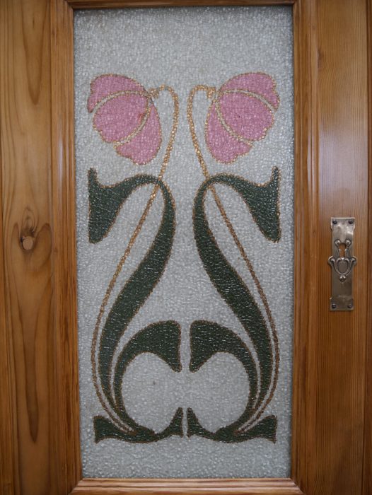 Detailaufnahme einer originalen Jugendstil-Glasscheibe mit floraler Bemalung in Schwarz, Grün und Rosa. Die kunstvolle Jugendstilmalerei gehört zur originalen Ausstattung des Buffets.