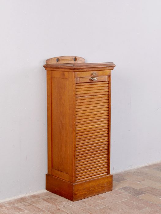 Frontansicht des originalen Rollschranks im geschlossenen Zustand. Der fein gearbeitete Rolladen, die schlichte Jugendstilgestaltung und der unrestaurierte Originalzustand sind gut erkennbar.
