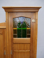Nahaufnahme des oberen Türbereiches mit originalem Jugendstil-Bleiglas. Das dekorative Bleiglas mit farbigen Glaselementen gehört zur originalen Ausstattung des Schranks.