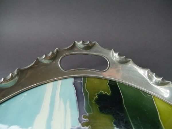 Detailaufnahme des reliefierten Metallrandes mit integriertem Griff. Die fein ausgearbeitete Ornamentik des Metallrahmens ergänzt die hochwertige Keramik und unterstreicht den dekorativen Charakter des Jugendstil-Tabletts.
