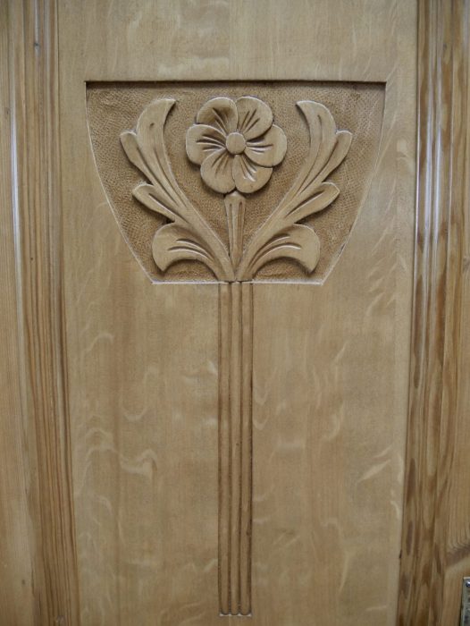 Nahaufnahme der kunstvoll geschnitzten Jugendstil-Ornamente auf der Türfüllung. Die floralen Schnitzereien sind typische Gestaltungselemente hochwertiger Jugendstil-Möbel.
