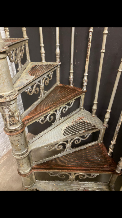 Blick von oben auf die spiralförmig angeordneten Treppenstufen der historischen Jugendstil-Spindeltreppe. Die charakteristische Wendelkonstruktion und die originale Patina sind besonders gut erkennbar.
