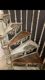 Blick von oben auf die spiralförmig angeordneten Treppenstufen der historischen Jugendstil-Spindeltreppe. Die charakteristische Wendelkonstruktion und die originale Patina sind besonders gut erkennbar.

