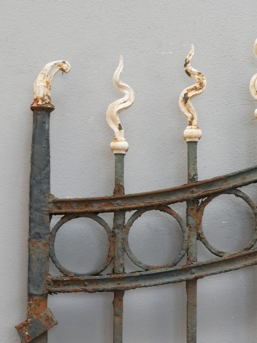 Detailaufnahme des geschwungenen oberen Torabschlusses mit dekorativen Schmiedespitzen und ringförmigen Ornamenten. Die hochwertige Schmiedearbeit ist typisch für repräsentative Jugendstil-Zaunanlagen.
