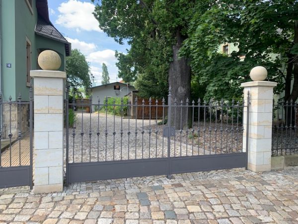 Gesamtansicht einer restaurierten historischen Schmiedeeisen-Zaunanlage mit großem Einfahrtstor. Das Bild veranschaulicht, wie die angebotene Jugendstil-Zaunanlage nach einer fachgerechten Restaurierung wirken kann.
