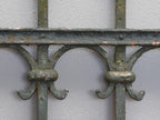 Detailaufnahme eines geschmiedeten Verbindungselements im unteren Bereich der Zaunanlage. Sichtbar sind die massiven Schmiedearbeiten und die originale handwerkliche Konstruktion des historischen Zauns.
