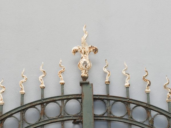 Detailaufnahme des geschwungenen oberen Torbogens mit dekorativen Schmiedeeisen-Ornamenten und eleganten Zierspitzen. Die kunstvolle Gestaltung unterstreicht den charakteristischen Jugendstil.
