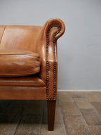 Nahaufnahme der rechten geschwungenen Rollenarmlehne mit dekorativen Ziernägeln und kräftiger Lederpatina. Das Detail zeigt die hochwertige handwerkliche Verarbeitung des Vintage-Ledersofas.

