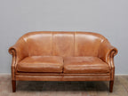 Frontansicht des Vintage-Ledersofas aus Schafsleder mit zwei großzügigen Sitzpolstern, elegant geschwungener Rückenlehne und warmem Cognac-Farbton. Die gleichmäßige Patina unterstreicht den authentischen Originalzustand.
