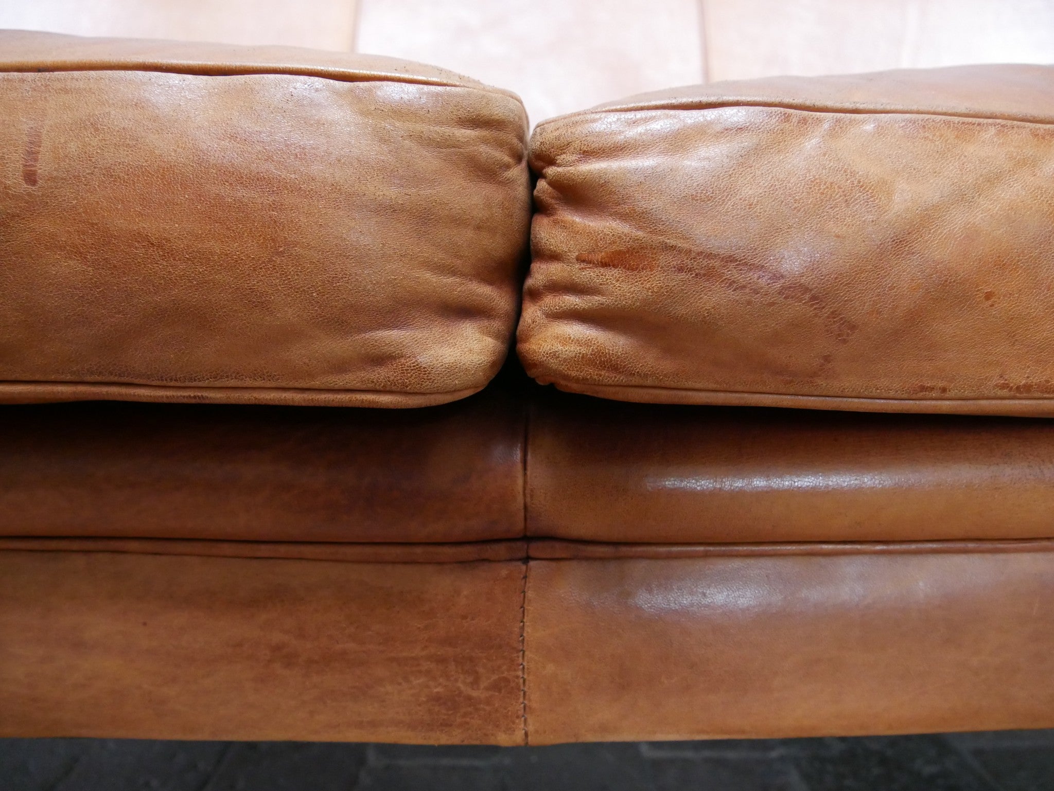Detailaufnahme des mittleren Sitzbereichs mit Übergang der beiden Sitzpolster. Sichtbar sind die originale Nahtführung, die natürliche Faltenbildung sowie die authentische Patina des hochwertigen Schafsleders.

