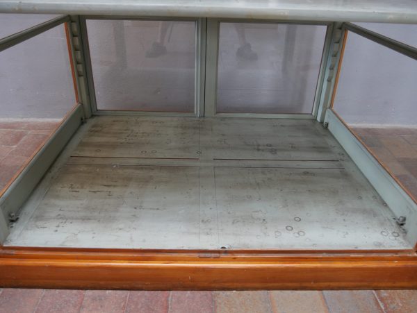 Detailaufnahme des unteren Innenbereichs mit original grau-grüner Bodenplatte und Holzrahmen. Die Aufnahme verdeutlicht den außergewöhnlich gut erhaltenen Originalzustand der Vitrine.