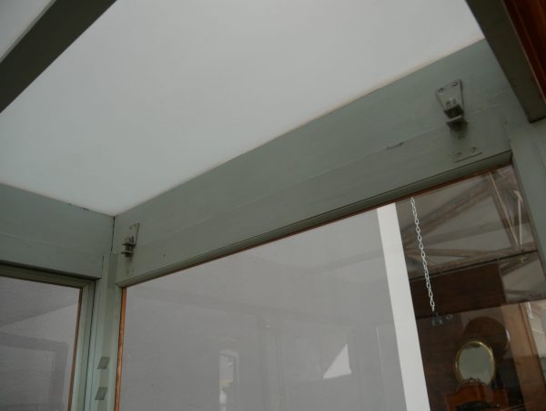 Detailaufnahme einer oberen Glasecke mit original mundgeblasenen Glasscheiben und fein gearbeiteten Holzprofilen. Die Aufnahme zeigt die hochwertige Verarbeitung der historischen Vitrine.