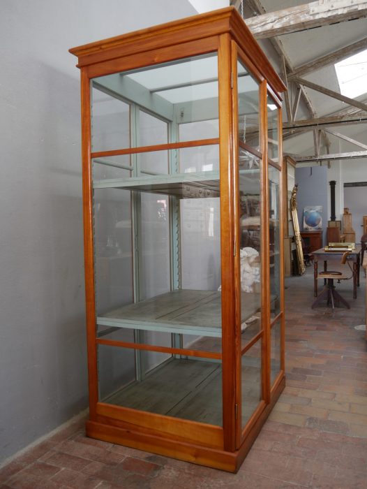 Schräg fotografierte Seitenansicht der vollständig verglasten Lehrmittelvitrine. Die elegante Konstruktion und die großzügigen Glasflächen machen den Schrank ideal für Präsentationszwecke.