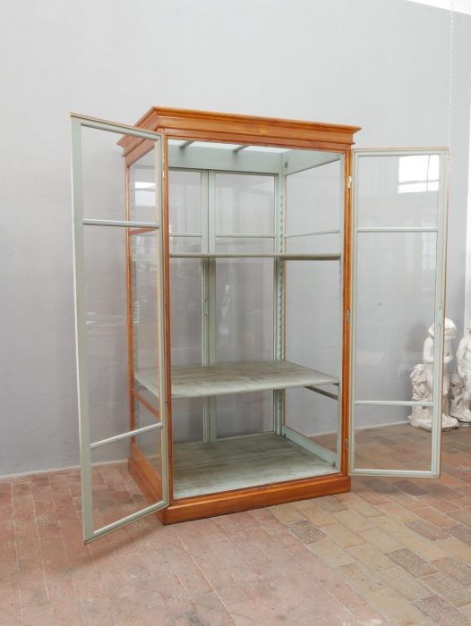 Lehrmittelschrank mit geöffneten Glastüren. Die Aufnahme zeigt den großzügigen Innenraum mit den beiden höhenverstellbaren Einlegeböden und der originalen grau-grünen Innenlackierung.