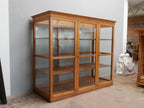 Schräg aufgenommene Seitenansicht der historischen Lehrmittelvitrine. Die Aufnahme zeigt die vollständig verglaste Konstruktion und die hochwertige Verarbeitung des originalen Weichholzschrankes.