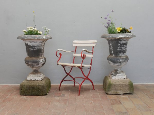 Hauptansicht eines außergewöhnlich seltenen Paars französischer Amphorenvasen aus massivem Gusseisen, entstanden um 1830. Die originalen Gartenvasen besitzen eine wunderschöne historische Patina mit erhaltenen Farbresten und stehen auf passenden Sandsteinsockeln, die optional erhältlich sind. Einst schmückten diese eleganten Amphoren eine französische Villa und zählen heute zu gesuchten Sammlerstücken.
