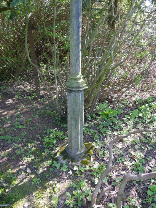 Detailaufnahme des unteren Bereichs einer gusseisernen Laterne mit schlankem Laternenmast und originalem Sockel im historischen Garten.