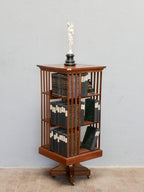 Schräge Frontansicht des drehbaren Jugendstil-Bücherkarussells aus massivem Nussbaum. Gut sichtbar sind die offenen Bücherfächer, die elegante Konstruktion mit senkrechten Streben sowie der massive drehbare Mittelfuß.
