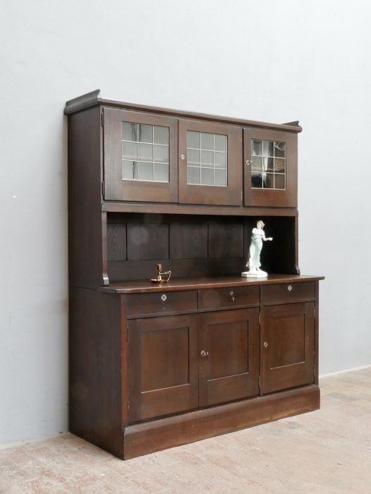 Seltenes originales Buffet bzw. Anrichte nach einem Entwurf von Richard Riemerschmid, ausgeführt 1909 in den Dresdner Werkstätten Hellerau. Die Hauptansicht zeigt das zweiteilige Möbel aus dunkel gebeizter Eiche mit originalem Glas, vernickelten Beschlägen, zwei Stangenschlössern und den sachlichen, für Riemerschmid typischen Gestaltungselementen.