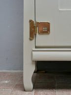 Detailaufnahme des unteren Seitenbereichs mit Möbelfuß, Sockel und originalem Messingbeschlag. Die leicht konische Bauweise des Schranks ist gut erkennbar.