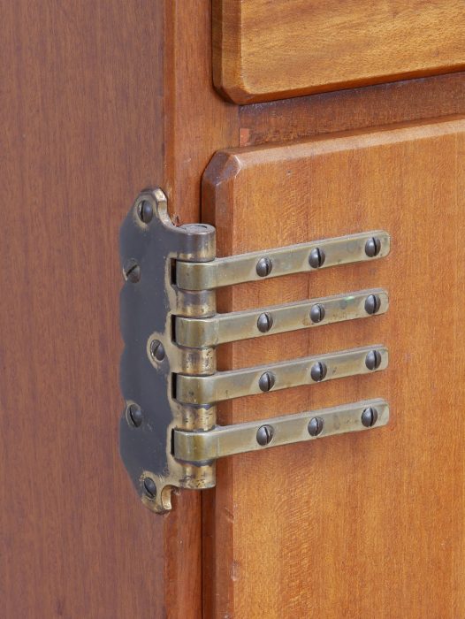 Detailaufnahme des originalen mehrteiligen Messingscharniers am Jugendstil-Schreibtisch von Richard Riemerschmid. Die präzise gearbeitete Beschlagtechnik der Deutschen Werkstätten Dresden-Hellerau dokumentiert die außergewöhnliche handwerkliche Qualität und den authentischen Originalzustand des Mahagoni-Möbels.
