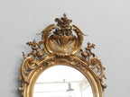 Detailaufnahme der reich ornamentierten Bekrönung des original stuckvergoldeten Standspiegels. Fein ausgearbeitete florale Schnitzereien, Blattwerk und geschwungene Zierelemente dokumentieren die hochwertige handwerkliche Ausführung des Spiegelrahmens.