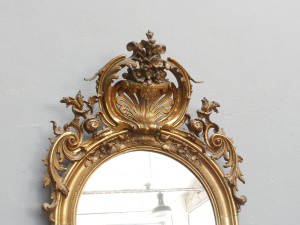 Detailaufnahme der reich ornamentierten Bekrönung des original stuckvergoldeten Standspiegels. Fein ausgearbeitete florale Schnitzereien, Blattwerk und geschwungene Zierelemente dokumentieren die hochwertige handwerkliche Ausführung des Spiegelrahmens.