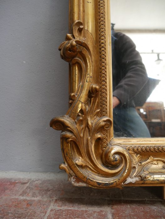 Nahaufnahme des unteren Eckbereiches mit kunstvoll geschnitzten Blatt- und Volutenornamenten. Die Aufnahme zeigt die feine Stuckvergoldung und die elegante Ausarbeitung des historischen Spiegelrahmens.