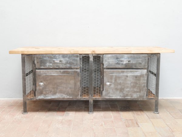Frontalansicht der restaurierten Werkbank mit symmetrischem Aufbau, originalen Metalltüren, Gittereinsätzen und massiver Holzarbeitsplatte.