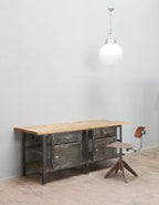 Schräge Vorderansicht der restaurierten Industrie-Werkbank mit geölter Original-Holzplatte, genieteten Metalltüren und authentischer Patina.