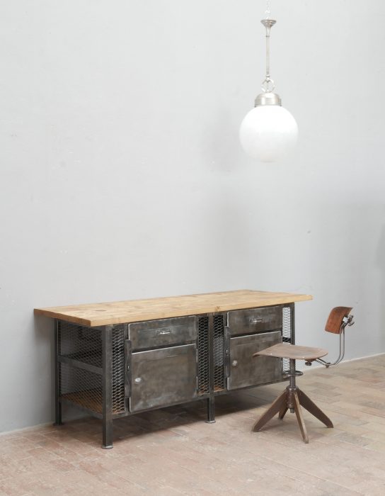 Schräge Vorderansicht der restaurierten Industrie-Werkbank mit geölter Original-Holzplatte, genieteten Metalltüren und authentischer Patina.