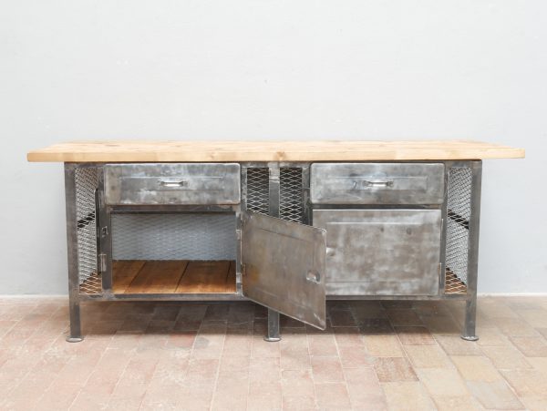 Historische Werkbank mit geöffneten Metalltüren. Sichtbar wird der großzügige Stauraum im restaurierten Unterbau mit neuer Holzbodenplatte im Stil des Originals.