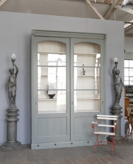 Gesamtansicht einer außergewöhnlichen XXL Bibliothek, Bücherschrank und Vitrine um 1910. Der aufwendig restaurierte Schrank besitzt außen einen grau-blauen Farbton und innen cremeweiße Einlegeböden. Zwei große originale Schiebetüren mit mundgeblasenem Glas, originale Messing-Griffmulden und die imposante Größe machen dieses Möbelstück zu einem besonderen Blickfang.