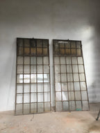 Zwei originale Fabrikfenster aus Schmiedeeisen um 1900 in der Gesamtansicht. Gut erkennbar sind die filigranen Sprossen, die großzügigen Glasflächen sowie die oberen Oberlichter, die über eine Kettenmechanik geöffnet werden können. Historische Industriefenster für Sanierung, Denkmalpflege oder exklusive Bauprojekte mit authentischem Fabrikcharakter.