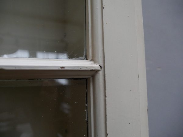 Detailaufnahme des alten mundgeblasenen Originalglases in einer Tür des historischen Lehrmittelschranks aus der Humboldt-Universität Berlin. Die leicht unregelmäßige Glasoberfläche und die altersbedingte Struktur unterstreichen den authentischen Originalzustand des Bücherschranks um 1910.