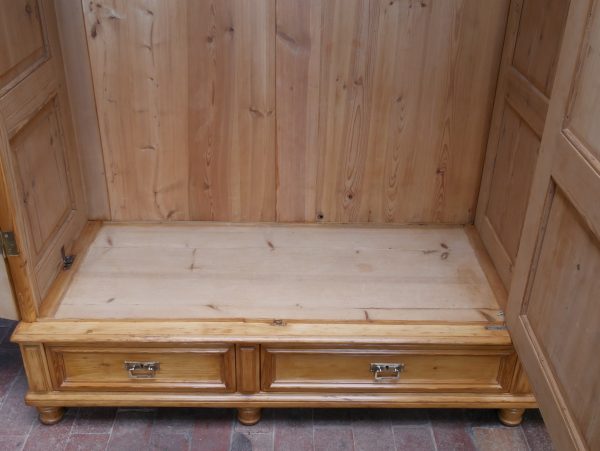 Detailaufnahme des unteren Innenbereichs des Schranks. Sichtbar sind der massive Holzboden, die Kleiderstange sowie die drei großen Schubladen im Sockelbereich, die von innen zugänglich sind.