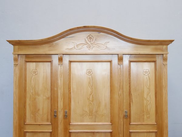 Detailaufnahme der elegant geschwungenen Kranzleiste mit geschnitztem Jugendstilornament. Die hochwertige handwerkliche Verarbeitung des restaurierten Schranks wird hervorgehoben.
