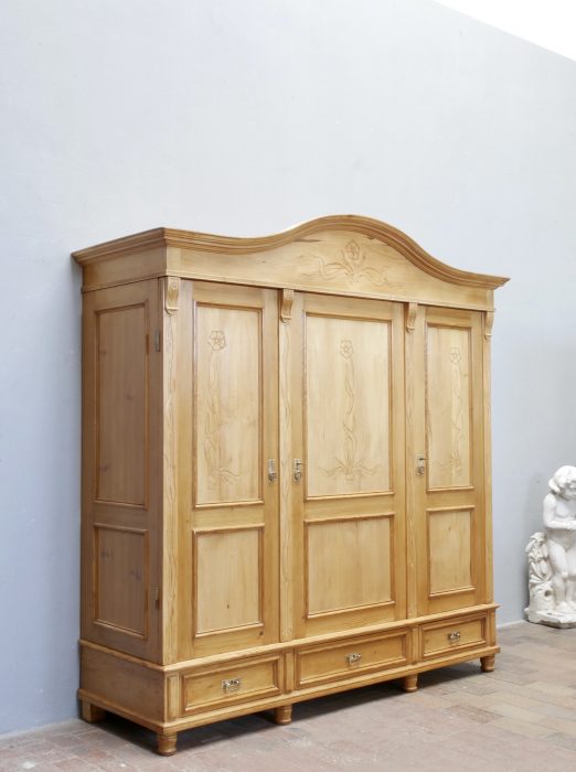 Schräge Vorderansicht des restaurierten XXXL Jugendstil-Kleiderschranks aus gewachster Kiefer. Gut sichtbar sind die harmonischen Proportionen, die geschweifte Kranzleiste und die aufwendig gearbeiteten Türfüllungen.